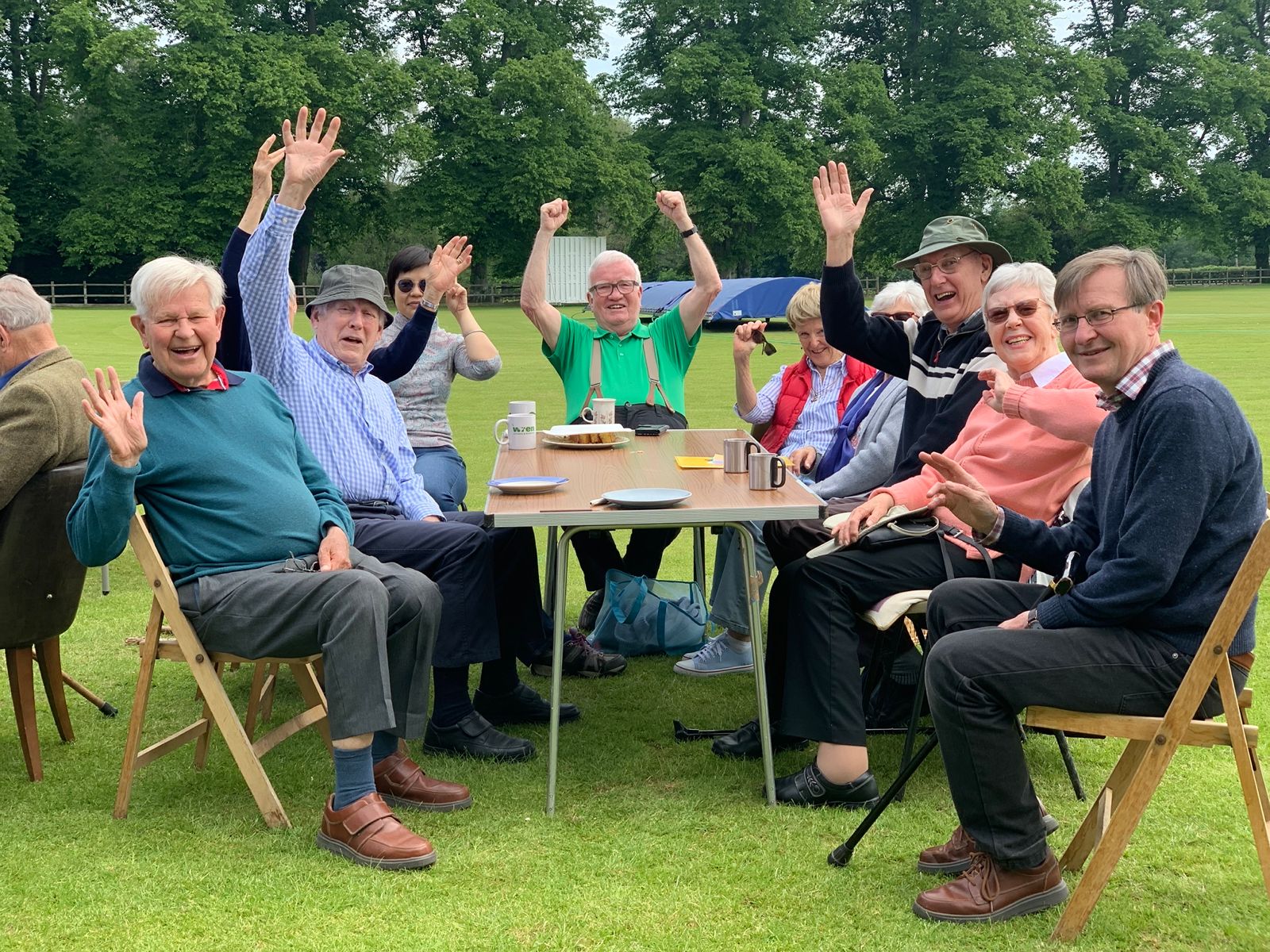 Chew Chatters waving and laughing around a table on the cricket ground